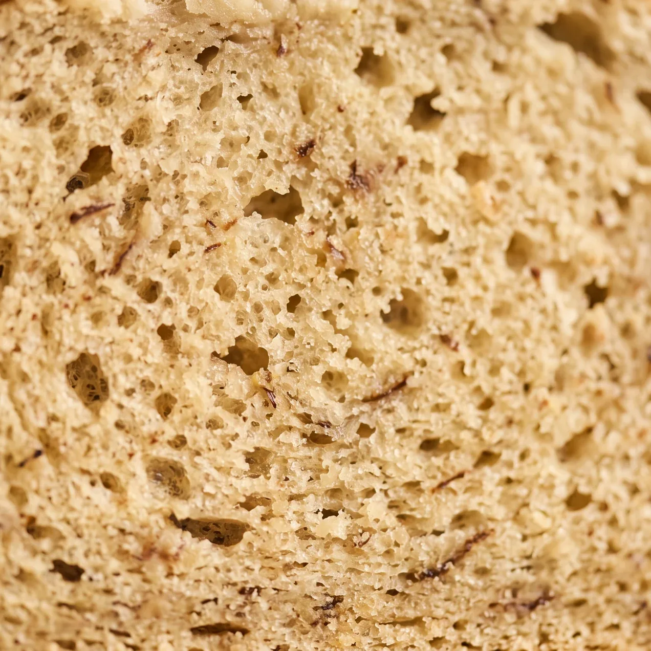 Extreme close-up of the centre of a banana bread slice, showing small irregular air pockets, flecks of banana, and a moist but fully set crumb.