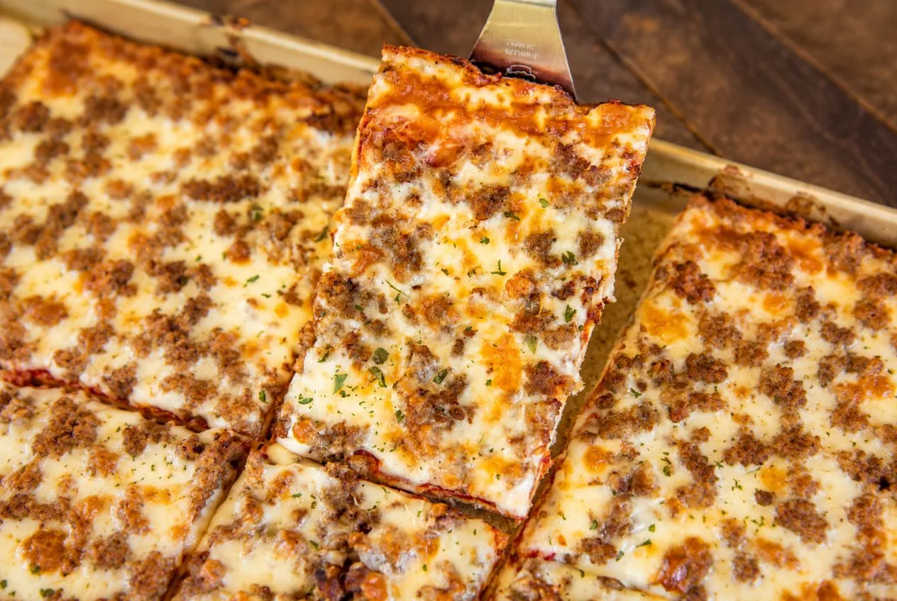 A rectangular slice of sausage school pizza lifted on a spatula from the cut pan