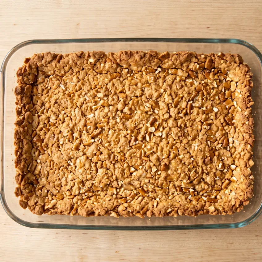 The baked pretzel crust pressed into a 9x13 glass dish, evenly golden and set, with individual pretzel pieces still visible on the surface.